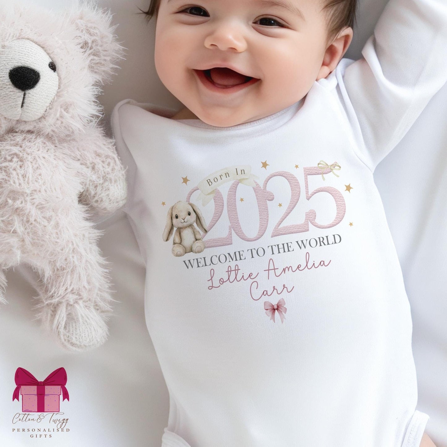 White cotton sleepsuit, vest & bib. born in 2025 featuring a gorgeous bunny design. welcome to the world, personalised with babys name. Pink writing.