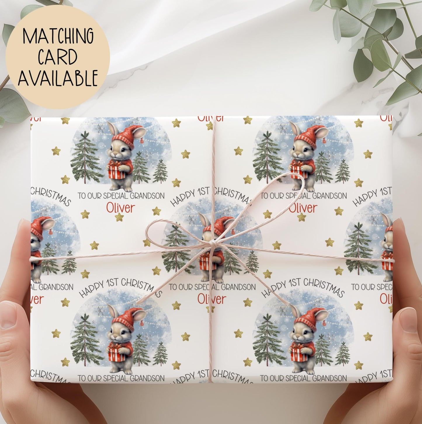 Personalised baby’s 1st Christmas Giftwrap for Boys & girls featuring a cute bunny in a red hat holding a present, snowy woodland background with fir trees and gold stars. Printed on premium 300gsm luxury paper.