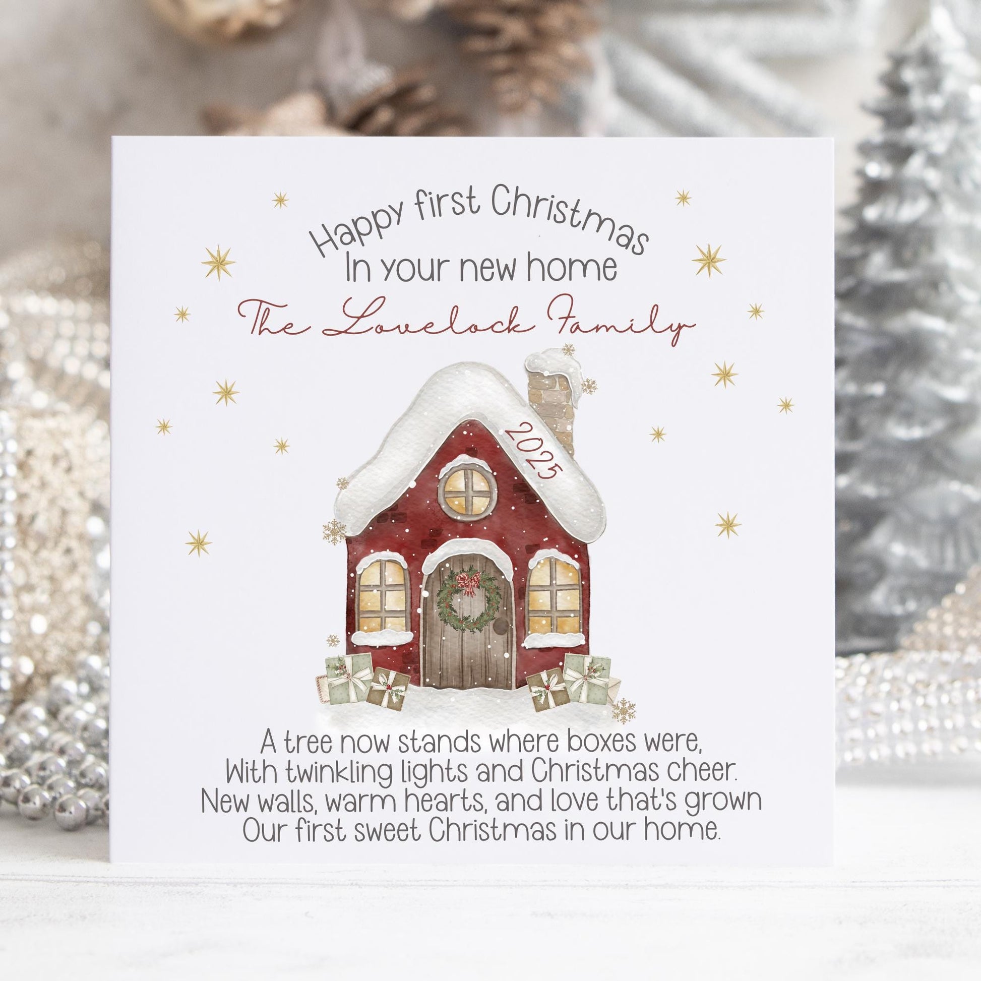 Personalised Christmas card featuring a cosy red snow-covered house with a wreath on the door and wrapped gifts outside. Surrounded by golden stars, the card reads “Happy First Christmas in Your New Home” and includes a short festive poem. The design can be customised with names and the year.