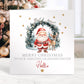 Personalised Christmas card featuring Santa and a reindeer standing in front of a festive wreath with twinkling lights, gold stars, and the message ‘Merry Christmas to our amazing granddaughter Hollie’ printed on the front. High-quality 300gsm card.