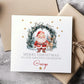 Personalised Christmas card featuring Santa and a reindeer standing in front of a festive wreath with twinkling lights, gold stars, and the message ‘Merry Christmas to our amazing granddaughter Hollie’ printed on the front. High-quality 300gsm card.