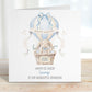 Square personalised Easter greeting card featuring a cute illustrated bunny sitting in a wicker hot air balloon basket surrounded by pastel Easter eggs. The balloon is decorated in soft blue tones with a ribbon and a banner reading ‘Happy Easter’. The design includes space for personalised text for name, year and relation.