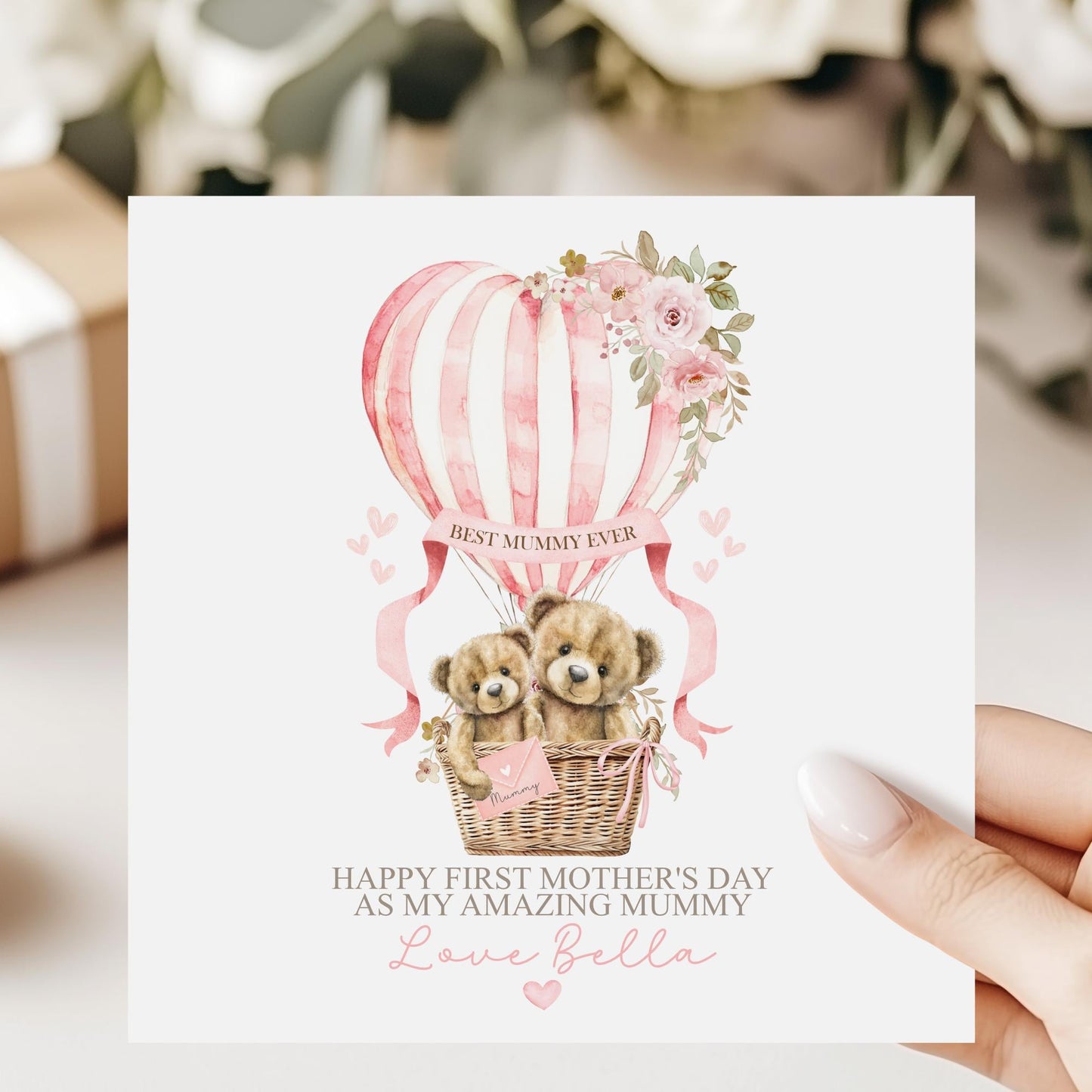 Personalised first Mother’s Day card for new mum, featuring two teddy bears in a wicker basket inside a pink hot air balloon with soft florals and hearts and the wording 'Happy 1st mothers day as my amazing mummy' Personalised with a name.