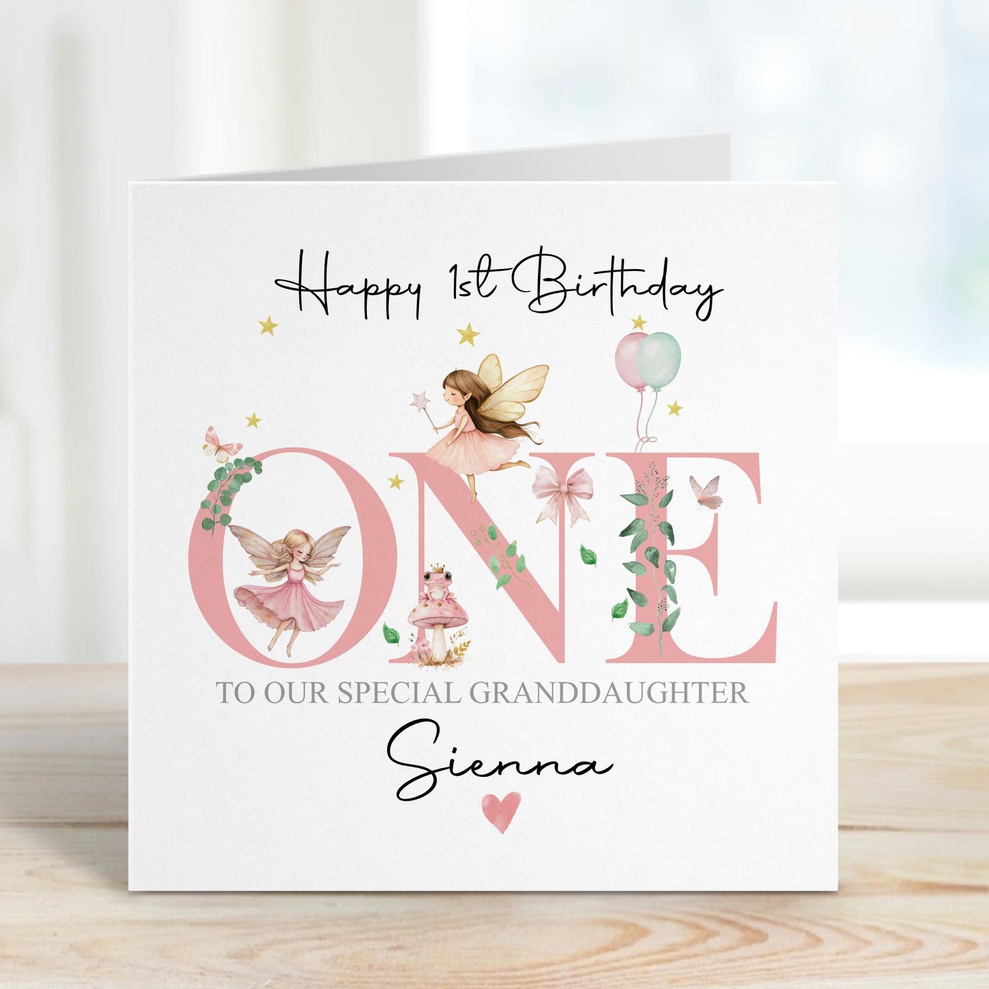 White linen luxury fairy 1st birthday card featuring beautiful little fairies & a pink toadstool & frog prince & the number one in pink & the wording Happy 1st birthday to our special daughter, granddaughter, niece, special little girl, can be adapted to any relation. Personalised with childs name.