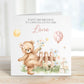 Square personalised third birthday greeting card featuring a cute illustrated teddy bear standing in a garden scene with flowers, a wooden fence, sunshine, gifts and a balloon showing the number three. The card includes personalised text for a child’s name and relation, with a soft pastel colour theme.