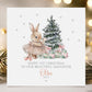 Personalised baby girl&#39;s 1st Christmas card featuring a cute bunny in a pink tutu holding a star wand, standing beside a snow-dusted Christmas tree with pink and green presents. Surrounded by silver stars, the card reads &#39;Happy 1st Christmas to our beautiful daughter 2025&#39; Personalised with childs name. A delicate and whimsical design perfect for a baby&#39;s first festive celebration