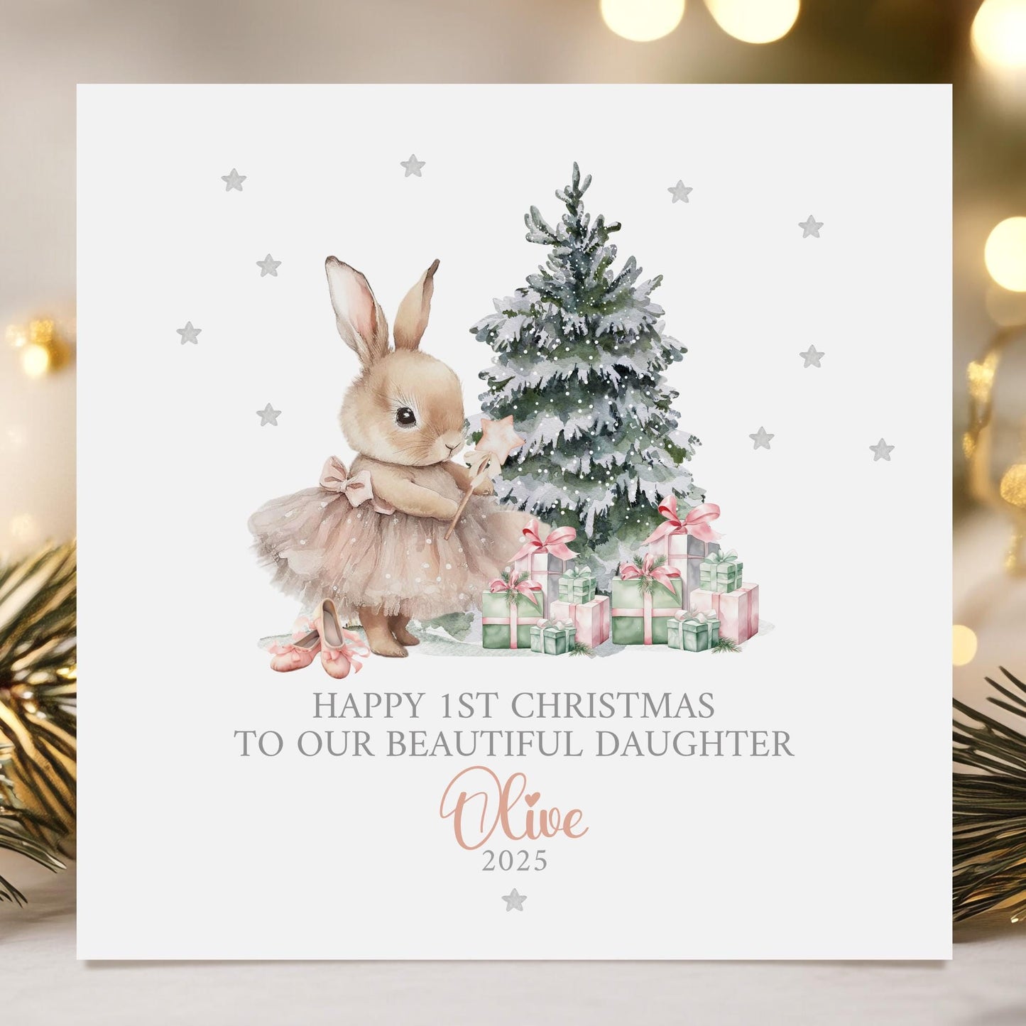 Personalised baby girl&#39;s 1st Christmas card featuring a cute bunny in a pink tutu holding a star wand, standing beside a snow-dusted Christmas tree with pink and green presents. Surrounded by silver stars, the card reads &#39;Happy 1st Christmas to our beautiful daughter 2025&#39; Personalised with childs name. A delicate and whimsical design perfect for a baby&#39;s first festive celebration