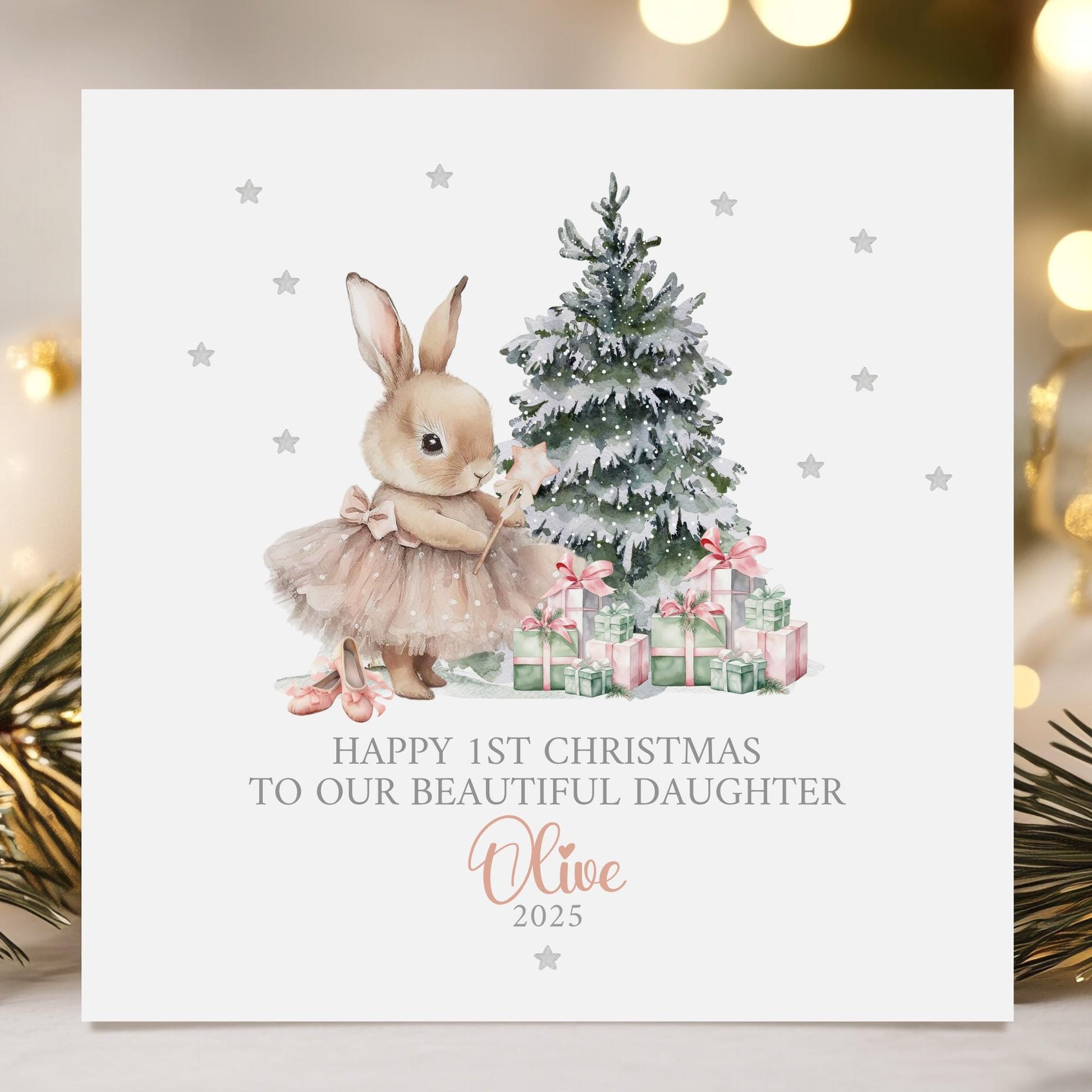 Personalised baby girl&#39;s 1st Christmas card featuring a cute bunny in a pink tutu holding a star wand, standing beside a snow-dusted Christmas tree with pink and green presents. Surrounded by silver stars, the card reads &#39;Happy 1st Christmas to our beautiful daughter 2025&#39; Personalised with childs name. A delicate and whimsical design perfect for a baby&#39;s first festive celebration