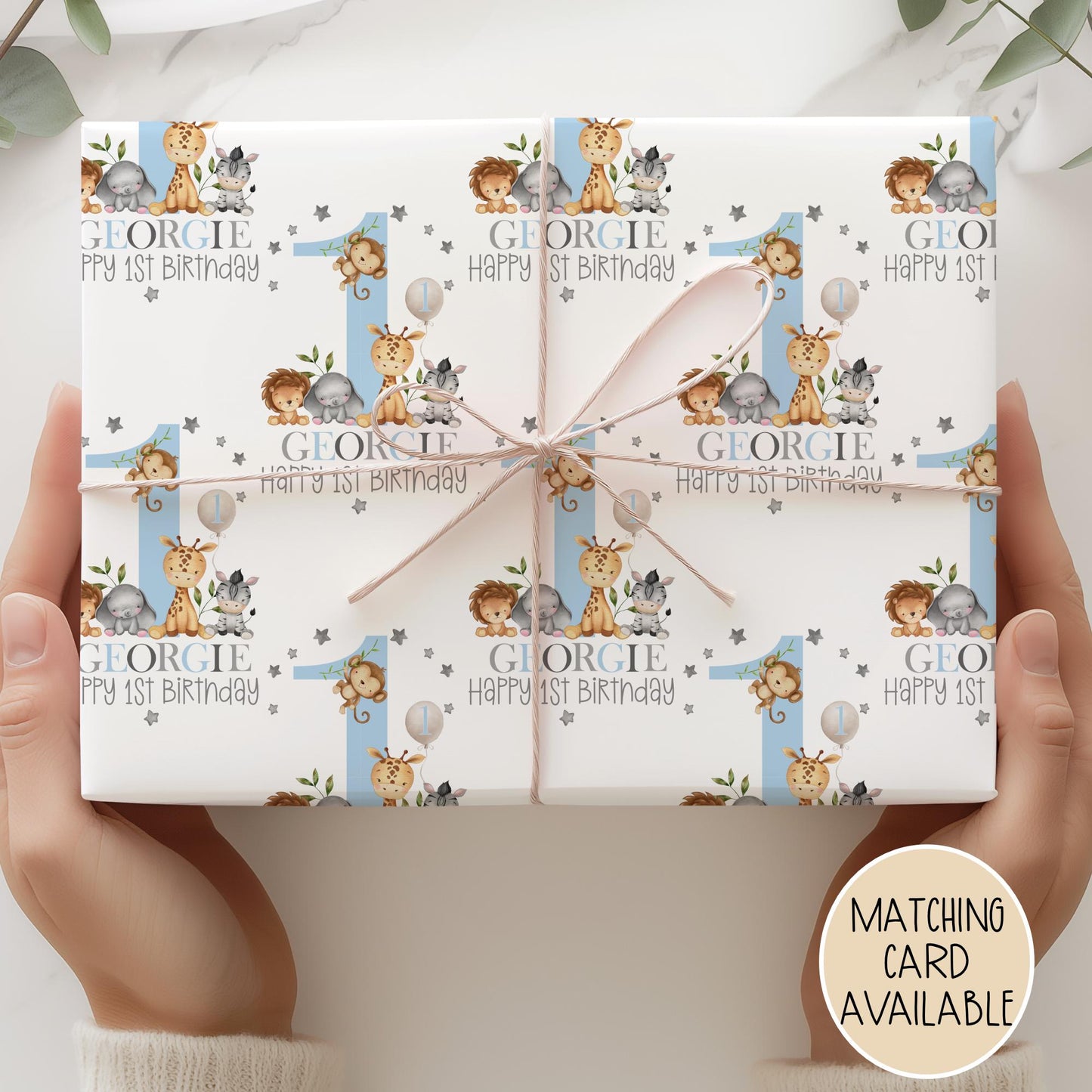Personalised gift wrap for a 1st birthday featuring a large blue number &#39;1&#39; surrounded by cute safari animals & grey stars. The design includes the text &#39; Happy 1st Birthday&#39; Personalised with a name in multi-coloured text.