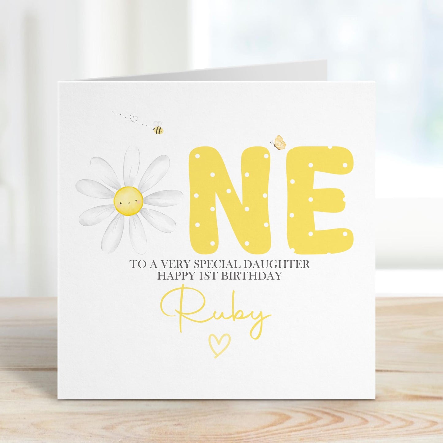 Luxury white linen, lightly textured 1st birthday card featuring a watercolor daisy & the one word ONE in yellow polka dot & pretty butterflys & a bee & the wording To a very special daughter, happy 1st birthday, personalised with the childs name a little heart. Card measures 6 x 6 inch