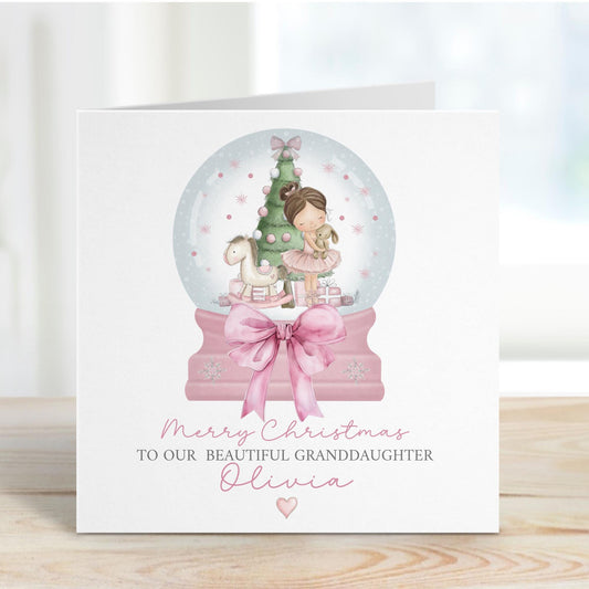 Square personalised Christmas card featuring a ballerina holding a teddy inside a pink snow globe with a Christmas tree, rocking horse, and presents. Text reads “Merry Christmas to our beautiful granddaughter/Daughter/Any relations&quot; Personalised with a name.
