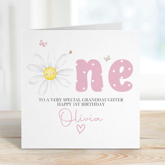 Luxury white linen, lightly textured 1st birthday card featuring a watercolor daisy & the one word ONE in pink polka dot & pretty butterflys & a bee & the wording To a very soecial granddaughter, happy 1st birthday, personalised with the childs name a little heart. Card measures 6 x 6 inches.