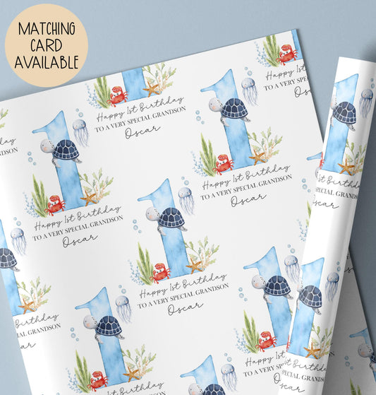 Personalised birthday gift wrap featuring a repeating watercolour design with a large blue number one, turtle, crab, jellyfish and sea plants, with “Happy 1st Birthday” text and space for a personalised name.