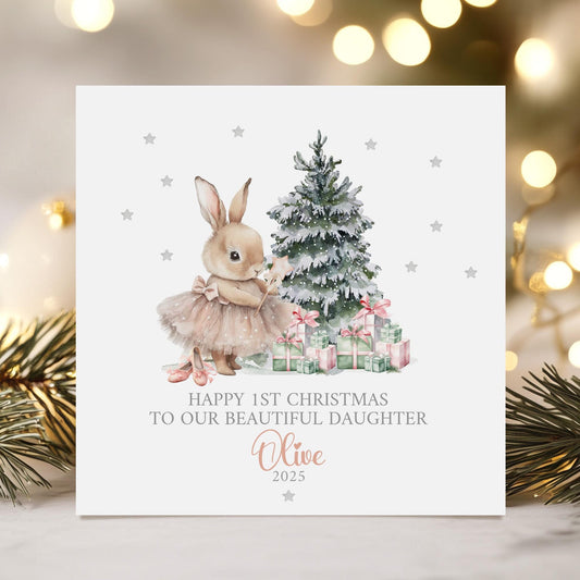 Personalised baby girl&#39;s 1st Christmas card featuring a cute bunny in a pink tutu holding a star wand, standing beside a snow-dusted Christmas tree with pink and green presents. Surrounded by silver stars, the card reads &#39;Happy 1st Christmas to our beautiful daughter 2025&#39; Personalised with childs name. A delicate and whimsical design perfect for a baby&#39;s first festive celebration